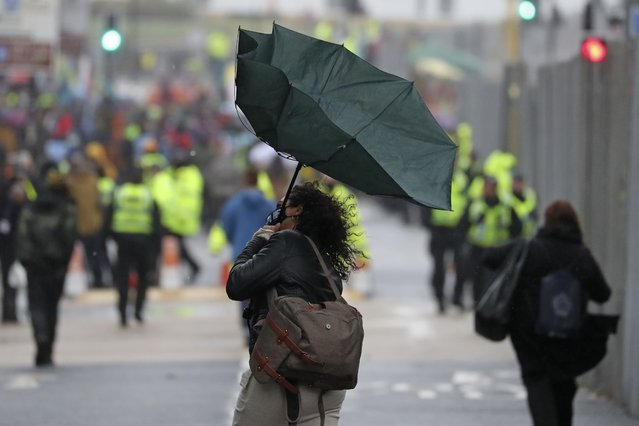 A woman's unbrella is turned inside out by a gust of wind outside the venue for the COP26 U.N. Climate Summit in Glasgow, Scotland, Friday, November 12, 2021. (Photo by Scott Heppell/AP Photo)