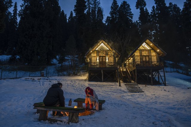 Tourists from Kenya sit by a bonfire outside a cottage in Drang village, northwest of Srinagar, Indian controlled Kashmir, Thursday, December 21, 2023. This is the time of “Chillai Kalan”, also called “The Great Winter”, a Kashmiri phrase which defines the harshest 40 days of cold in disputed Kashmir that commence in late December and extend into January and early February. Renowned for its breathtaking landscapes, Kashmir in winter transforms into a wonderland. Tourists fill its hotels to ski, sledge and trek the Himalayan landscape. (Photo by Dar Yasin/AP Photo)