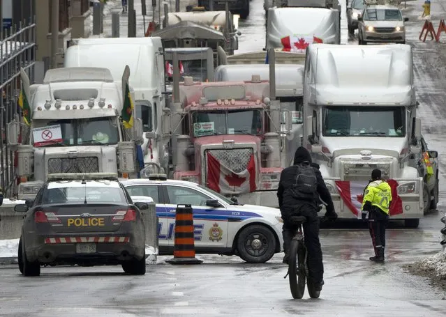 A cyclist rides towards a police barricade where trucks are lined up near Parliament hill on Wednesday, February 2, 2022 in Ottawa. Thousands of protesters railing against vaccine mandates and other COVID-19 restrictions descended on the capital, deliberately blocking traffic around Parliament Hill. (Photo by Adrian Wyld/The Canadian Press via AP Photo)