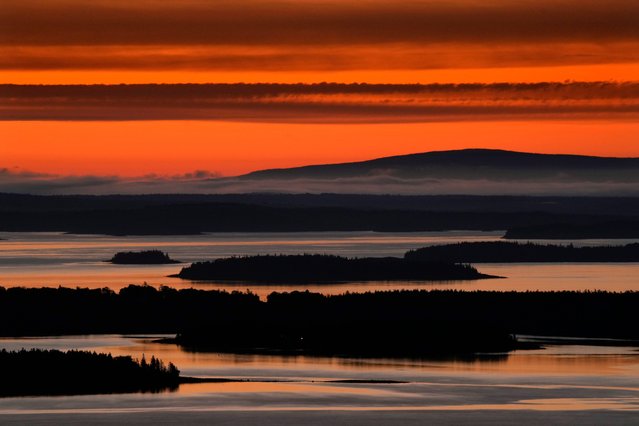 The predawn sky reflects in the calm waters of Penobscot Bay, Tuesday, June 4, 2024, near Camden, Maine. Cadillac Mountain, the highest point on the eastern seaboard at 1,527 feet, stands in the distance. (Photo by Robert F. Bukaty/AP Photo)