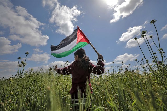 A Palestinian girl waves a Palestinian flag during a protest marking “Land Day” along the border between Israel and the Gaza Strip, in the east Gaza Strip, 30 March 2023. The day commemorates the 30 March 1976 events, when marches and a general strike was organized in Arab towns against the Israeli government's decision to expropriate large tracts of Palestinian-owned land for settlement. The annual event calls for the Palestinian right to return to the land they were displaced from after the creation of Israel in 1948. (Photo by Mohammed Saber/EPA)