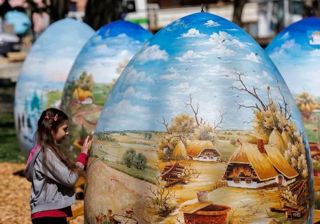 A girl looks at two-metre-high Easter eggs painted in the traditional naive art style in Koprivnica, Croatia, April 14, 2022. This project started fifteen years ago and involves painters decorating two-metre-tall polyester eggs, which are then sent to cities in the country and abroad to be displayed in public squares in time for Easter festivities. (Photo by Antonio Bronic/Reuters)