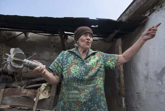 Tamara Kutnenko, 71, shows a part of a spent mortar shell next to her damaged house after recent shelling, on a territory controlled by Ukrainian army, some 15 km to the front line, in the urban village of Novotroitskoe, Donetsk area, Ukraine, 22 July 2015. Pro-Russian separatists have said they will withdraw all of their heavy weapons from the conflict zones of eastern Ukraine on 26 July in accordance with an agreement with the Organization for Security and Cooperation in Europe (OSCE). (Photo by Sergey Vaganov/EPA)