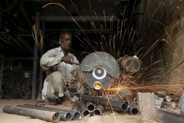 A technician uses an electric cutter to cut the pipes at a workshop in Karachi, Pakistan, July 25, 2015. (Photo by Akhtar Soomro/Reuters)