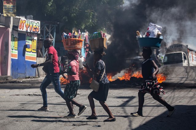 People carry their belongings as they move past a fire barricade during a protest against gang violence in the Solino neighborhood of Port-au-Prince, Haiti, 19 August 2024. (Photo by Mentor David Lorens/EPA/EFE)