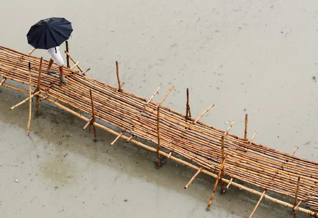 A man walks on a temporary bamboo bridge during heavy rains on the banks of river Ganga in Allahabad, India, June 22, 2016. (Photo by Jitendra Prakash/Reuters)