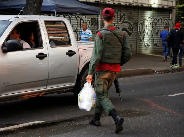 A Venezuelan soldier walks while holding a bag of food on a street in Caracas, Venezuela, June 23, 2016. (Photo by Mariana Bazo/Reuters)