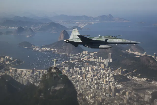 A F-5 fighter flies over the Christ the Redeemer statue, Guanabara Bay and the Sugar Loaf mountain, photographed through a window, while intercepting another aircraft during a Brazilian Air Force presentation for the press ahead of the Olympic games in Rio de Janeiro, Brazil, Thursday, July 14, 2016. (Photo by Felipe Dana/AP Photo)