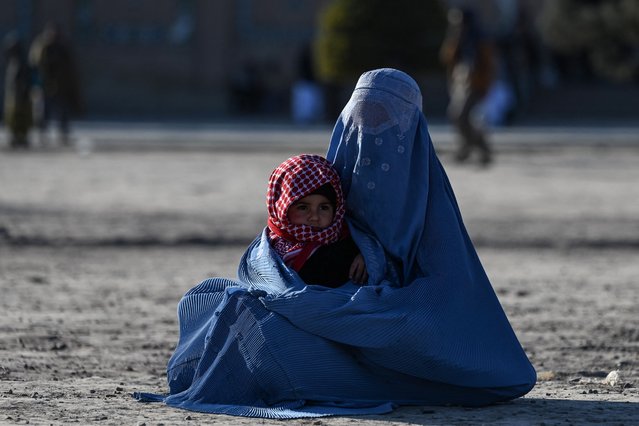 An Afghan burqa-clad woman holds a child as she asks for alms in front of the Great Mosque of Heart, in Herat on December 22, 2024. (Photo by Wakil Kohsar/AFP Photo)
