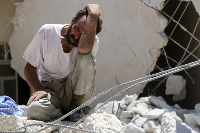 A man looks on as Syrian civil defense workers look for survivors under the rubble of a collapsed building following reported air strikes on July 17, 2016 in the rebel-controlled neighbourhood of Karm Homad in the northern city of Aleppo. Opposition-controlled parts of Syria's battered northern city Aleppo came under total siege, after government forces severed the last route out of the east. An estimated 300,000 civilians live in rebel-held neighbourhoods of Syria's second city, according to the United Nations, and there are fears that they could face starvation. (Photo by Thaer Mohammed/AFP Photo)