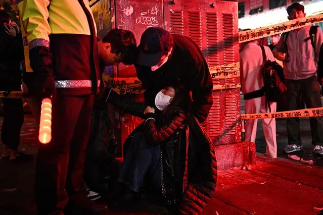 A woman is attended to as dozens of people suffered cardiac arrest in the popular nightlife district of Itaewon in Seoul on October 30, 2022. Dozens of people suffered from cardiac arrest in the South Korean capital Seoul, after thousands of people crowded into narrow streets in the city's Itaewon neighbourhood to celebrate Halloween, local officials said. (Photo by Anthony Wallace/AFP Photo)