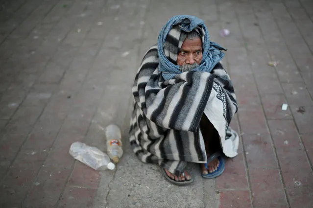 A man is covered in a quilt to keep himself warm as he sits on a pavement on a cold winter morning in New Delhi, India November 22, 2017. (Photo by Adnan Abidi/Reuters)