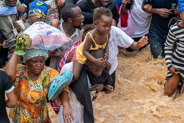 Residents wade through murky floodwaters following heavy rains in the Ndjili district of Kinshasa on April 6, 2025. (Photo by Hardy Bope/AFP Photo)