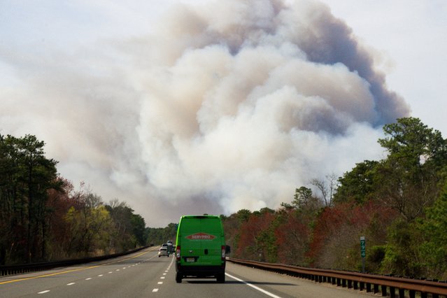 Vehicles drive as smoke rises during a wildfire outbreak in Bayville, in the Ocean County region of New Jersey on April 23, 2025. (Photo by Eduardo Munoz/Reuters)