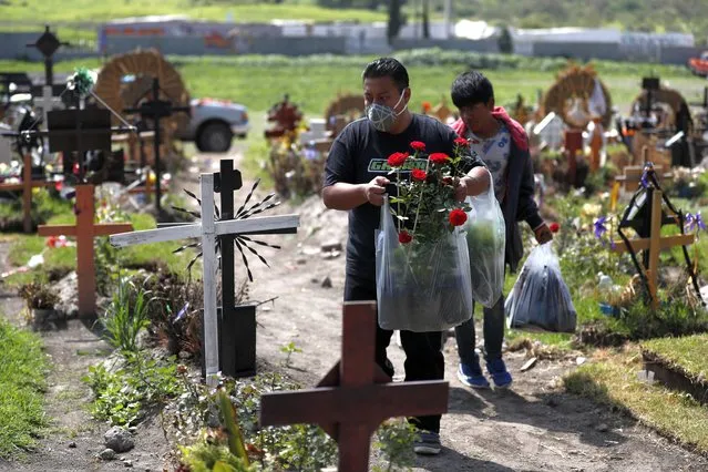 Men carry flowers as family members arrive to decorate the grave of a man who died of suspected COVID-19, in a section of the Municipal Cemetery of Valle de Chalco opened three months ago to accommodate the surge in deaths amid the ongoing new coronavirus pandemic, on the outskirts of Mexico City, Friday, August 7, 2020. Mexico on Thursday jumped above 50,000 recorded deaths from COVID-19, the third-highest death toll in the world, behind only the United States and Brazil. (Photo by Rebecca Blackwell/AP Photo)