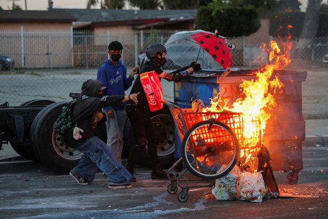 Protesters stand next to a burning shopping cart during a standoff between police and protesters following multiple detentions by ICE, in the Los Angeles County city of Compton, California, U.S., June 7, 2025. (Photo by Daniel Cole/Reuters)