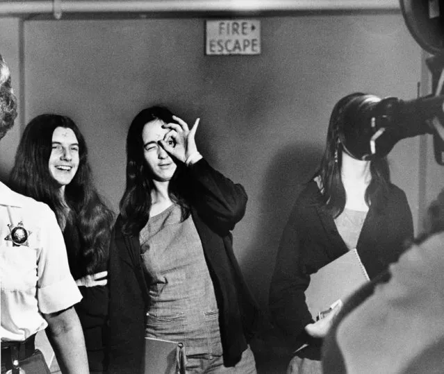 Susan Denise Atkins, defendant in the Tate murder trial, mimics a television film cameraman while on her way to court in Los Angeles with fellow defendants Patricia Krenwinkel, left, and Leslie Van Houten, hidden by the camera lens, September 22, 1970. (Photo by AP Photo)