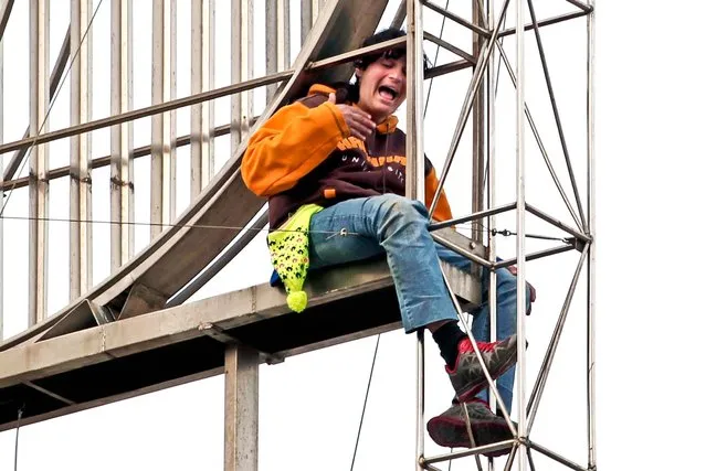 A 35-year-old deaf and mute woman threatens to take her life after climbing up the supports of a sculpture in Omonia Square, Athens, on March 11, 2013. The woman, a single mother of two, was protesting serious delays in disability payments that have resulted from successive austerity measures in the crisis-hit country. The woman was later lifted to safety by fire fighters using a crane. She had carried out a similar protest at the same spot three months ago. (Photo by Petros Giannakouris/Associated Press)