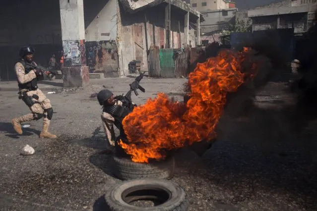 A National Police officer slips while trying to kick a burning tire at a barricade set up by protesters demanding the resignation of President Michel Martelly, in Port-au-Prince, Haiti, Friday, November 28, 2014. (Photo by Dieu Nalio Chery/AP Photo)
