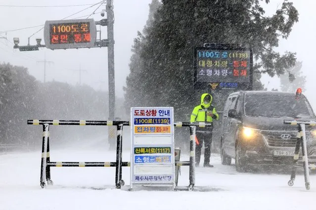 A police officer controls the entry of vehicles at a road amid heavy snowfall on Jeju Island, South Korea, Tuesday, January 24, 2023. Thousands of travelers swarmed a small airport in South Korea's Jeju island on Wednesday in a scramble to get on flights following delays by snowstorms as frigid winter weather gripped East Asia for the second straight day. (Photo by Park Ji-ho/Yonhap via AP Photo)
