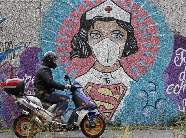 A man on a scooter passes a graffiti by street artist “Uzey”, depicting a nurse as superhero in the coronavirus pandemic on a wall in Hamm, Germany, Monday, September 28, 2020. The city of Hamm is the number one coronavirus hotspot at the moment in Germany, with a sudden increase of Covid-19 infections. Most of them are related to a wedding with more than 300 guests. (Photo by Martin Meissner/AP Photo)
