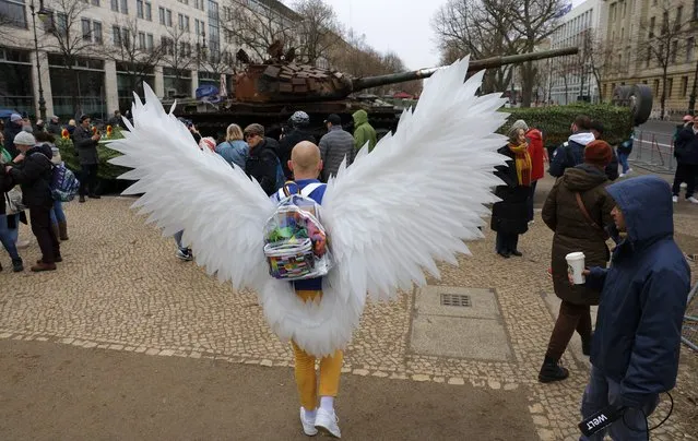 A man dressed in the colors of Ukraine and wearing white wings is seen in front of a Russian T-72 tank destroyed in Ukraine that is installed close to Russia's embassy in Berlin on February 24, 2023, on the first anniversary of the invasion of Ukraine. The wrecked tank was placed as an art installation by the “Berlin Story Bunker” group in front of the Russian embassy as “a symbol of Russia's downfall”. (Photo by Odd Andersen/AFP Photo)