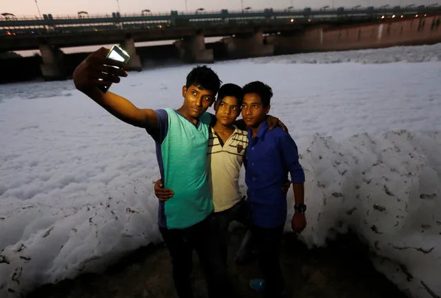 Boys pose for a selfie in front of the foam covering the polluted Yamuna river in New Delhi, India, October 11, 2016. (Photo by Adnan Abidi/Reuters)