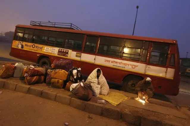 A couple wrapped in quilts wait for their bus at a terminal on a cold winter morning in New Delhi December 23, 2014. (Photo by Adnan Abidi/Reuters)