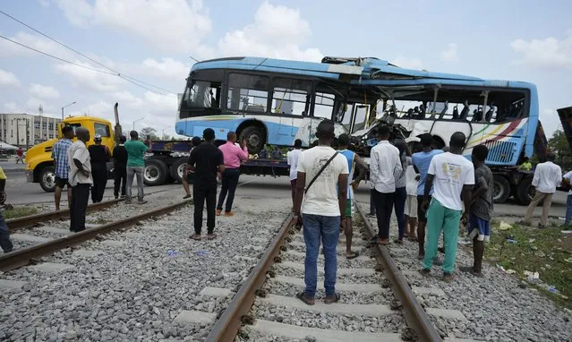 People watch as the the wreckage of a bus that was crushed by a train is been towed in Ikeja Lagos, Nigeria, Thursday, March. 9, 2023. Three people were killed and more than 80 injured after a passenger bus was crushed by a moving train in Nigeria's commercial hub of Lagos, the emergency response agency said on Thursday. (Photo by Sunday Alamba/AP Photo)