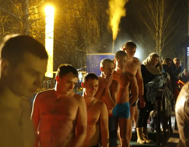 People watch as a man swims in the ice cold water of a lake on the eve of Russian Orthodox Epiphany in Minsk, Belarus, late Sunday, January 18, 2015. (Photo by Sergei Grits/AP Photo)