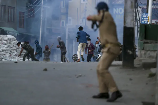 Kashmiri Muslim protesters run for cover as a policeman fires pellet gun at them during a protest against the killing of civilians, in Srinagar, Indian controlled Kashmir, Saturday, July 7, 2018. Two young men and a teenage girl were killed in disputed Kashmir on Saturday when government forces fired at anti-India protesters, police and medics said. (Photo by Dar Yasin/AP Photo)