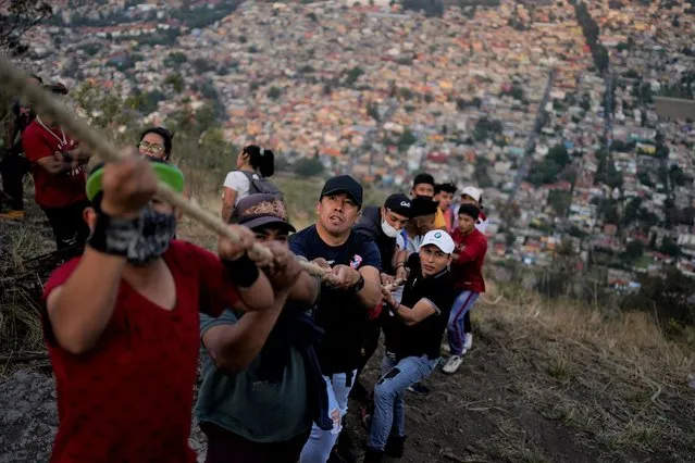 People work to lower a heavy, wooden cross from a hilltop as part of celebrations marking the day of the Holy Cross, in the Santa Cruz Xochitpec neighborhood of Mexico City, late Monday, May 2, 2022. The importance of the fabric-draped cross is reflected in the town's very name, which means “Holy Cross of the Flowered Hill”. (Photo by Eduardo Verdugo/AP Photo)