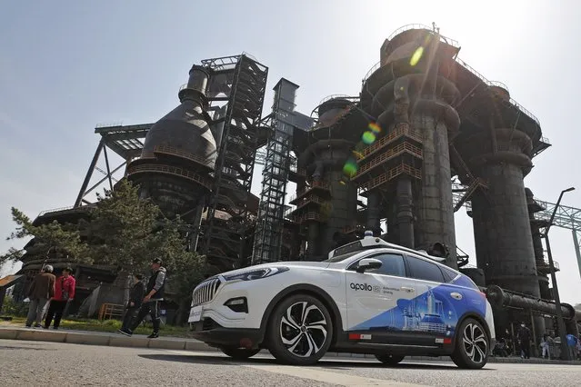 A Baidu Apollo Robotaxi move past a steel plant at the Shougang Park in Beijing, Sunday, May 2, 2021. Chinese tech giant Baidu rolled out its paid driverless taxi service on Sunday, making it the first company that commercialized autonomous driving operations in China. (Photo by Andy Wong/AP Photo)