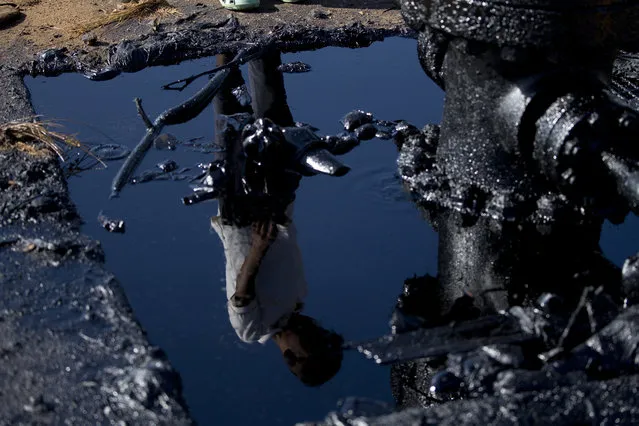 In this August 20, 2018 photo, a boy is reflected in a puddle of crude spilling from a well in Cabimas on the outskirts of Maracaibo, Venezuela. Broken down oil platforms span the vast Maracaibo Lake, with downwind shores soaked in oil. (Photo by Fernando Llano/AP Photo)