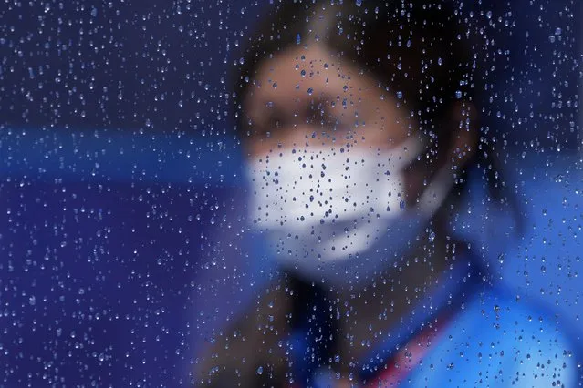 A masked worker walks by a rain-covered window after a rain storm at a field hockey match at the 2020 Summer Olympics, Tuesday, July 27, 2021, in Tokyo, Japan. (Photo by John Locher/AP Photo)