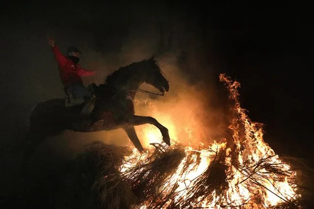 A man rides a horse through a bonfire as part of a ritual in honor of Saint Anthony the Abbot, the patron saint of domestic animals, in San Bartolome de Pinares, Spain, Tuesday, January 16, 2024. On the eve of Saint Anthony's Day, dozens ride their horses through the narrow cobblestone streets of the small village of San Bartolome during the “Luminarias”, a tradition that dates back 500 years and is meant to purify the animals with the smoke of the bonfires and protect them for the year to come. (Photo by Bernat Armangue/AP Photo)