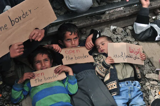 Children lie on railway track as they hold banners reading “Open the border” during a demonstration near the makeshift camp close to the Greek village of Idomeni by the Greek-Macedonian border where thousands of refugees and migrants are trapped by the Balkan border blockade, on March 12, 2016. Greece aims to deal swiftly with the migrant overflow at the Idomeni refugee camp on the Greek-Macedonian border where some 12,000 people are camping in miserable conditions waiting to cross. (Photo by Sakis Mitrolidis/AFP Photo)