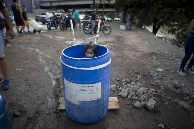 A little girl stands inside a plastic barrel while her family waits to collect water from an open pipe above the Guaire River, during rolling blackouts which affect the water pumps in people's homes, offices and stores, in Caracas, Venezuela, Monday, March 11, 2019. The blackout has intensified the toxic political climate, with opposition leader Juan Guaido blaming alleged government corruption and mismanagement and President Nicolas Maduro accusing his U.S.-backed adversary of sabotaging the national grid. (Photo by Ariana Cubillos/AP Photo)