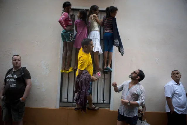 People climb a window grate as they get wet in the rain, in hopes of catching a glimpse of President Barack Obama during his visit to Cathedral Square in Old Havana, Cuba, Sunday, March 20, 2016. (Photo by Rebecca Blackwell/AP Photo)