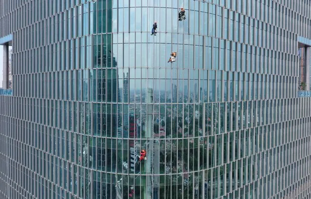 This aerial photo shows workers cleaning the windows of a high-rise building in Jakarta on December 14, 2021. (Photo by Adek Berry/AFP Photo)