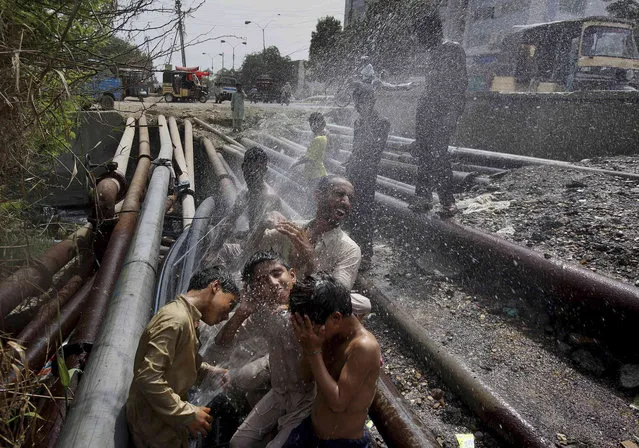 People cool themselves off in spray from broken water pipes at a road side in Karachi, Pakistan, where temperature reached above 42 degrees Celsius (108 Fahrenheit), Thursday, June 13, 2019. The meteorological department Thursday issued an alert, warning fishermen to avoid fishing in the Arabian sea this week as the Cyclone Vayu could cause rough conditions in the sea. (Photo by Fareed Khan/AP Photo)