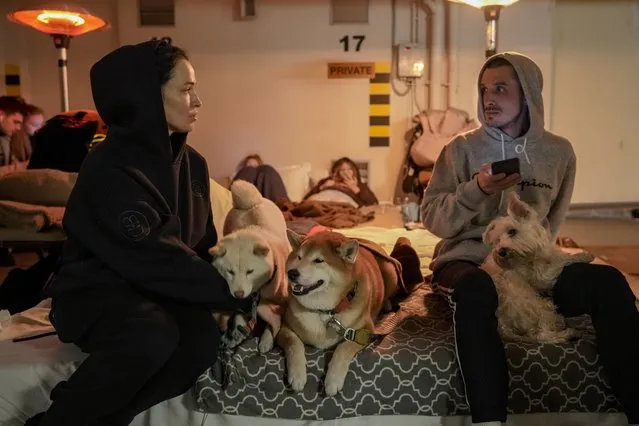 A couple and their dogs sit in a hotel underground parking turned into a bomb shelter during an air raid alert in Kyiv, Ukraine, Sunday, February 27, 2022. Terrified men, women and children sought safety inside and underground, and the government maintained a 39-hour curfew to keep people off the streets as more than 150,000 Ukrainians fled to neighboring countries and the United Nations warned the number could grow to 4 million if fighting escalates. (Photo by Vadim Ghirda/AP Photo)