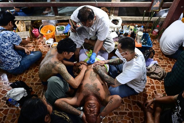 A Buddhist devotee (C) gets a traditional “Sak Yant” tattoo during an annual sacred tattoo festival at the Wat Bang Phra temple in Nakhon Pathom province, Thailand on March 4, 2023. (Photo by Manan Vatsyayana/AFP Photo)