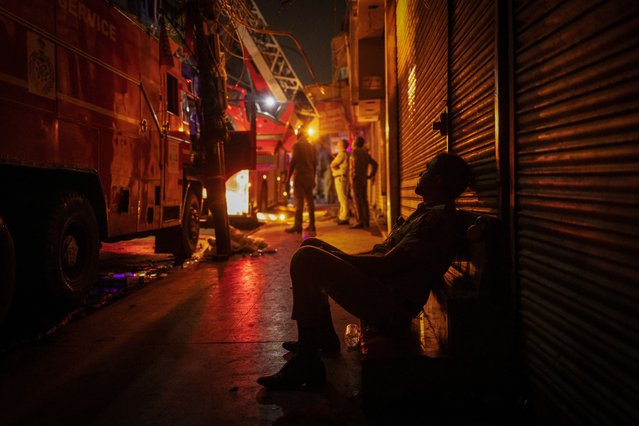 An exhausted firefighter sits next to a fire truck during an ongoing fire in some textile shops at a market area in the old quarters of Delhi, India, June 13, 2024. (Photo by Adnan Abidi/Reuters)