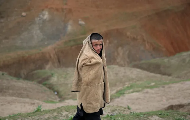 In this Sunday, May 4, 2014 photo, An Afghan teenager protects himself from the rain as he walks near the site of Friday's landslide that buried Abi-Barik village in Badakhshan province, northeastern Afghanistan. Stranded and with no homes, many of the families have struggled to get aid. Some have gone to nearby villages to stay with relatives or friends, while others have slept in tents provided by aid groups. (Photo by Massoud Hossaini/AP Photo)