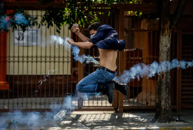 An opposition activist thows a stone at riot police during clashes following a protest against President Nicolas Maduro in Caracas on April 26, 2017. Venezuelan riot police fired tear gas to stop anti-government protesters from marching on central Caracas, the latest clash in a wave of unrest that, up to now, has left 26 people dead. (Photo by Federico Parra/AFP Photo)