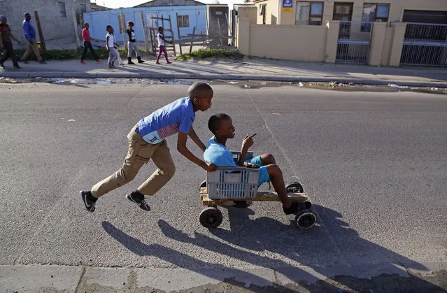 In this Monday, July 6, 2015 photo, a child pushes a friend in a home-made go-kart in the Khayelitsha township near Cape Town, South Africa. The vehicle was built with recycled wood, plastic containers and old nails. (Photo by Schalk van Zuydam/AP Photo)