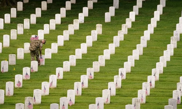 A soldier of the 3rd U.S. Infantry Regiment (The Old Guard) places flags on headstones ahead of Memorial Day, an annual ceremony where over one thousand soldiers place small American flags at more than 260,000 headstones at Arlington National Cemetery, in Arlington, Virginia, U.S., May 26, 2022. (Photo by Kevin Lamarque/Reuters)