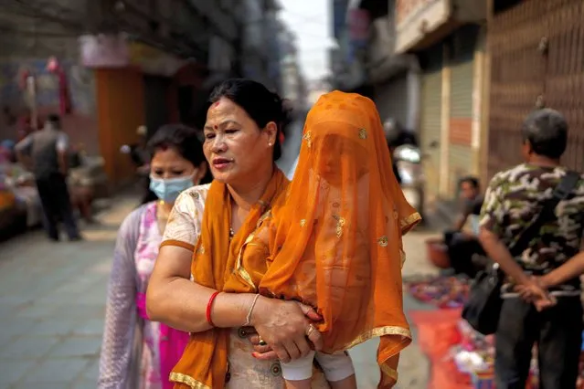 A Nepalese woman walks carrying a child covered with a piece of cloth to protect from dust and pollution in Kathmandu, Nepal, Tuesday, April 26, 2022. (Photo by Niranjan Shrestha/AP Photo)