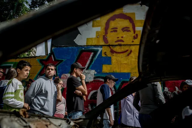 People wait in a line in front a graffiti as a kid of deceased president Hugo Chavez in Caracas, Venezuela on June 24, 2016. The line leads  to certify the authenticity of petitioners' signatures, in the National Electoral Center headquarters  in Caracas. The opposition is pushing for a recall referendum this year to cut short President Nicolas Maduro's term and trigger new elections. (Photo by Alejandro Cegarra/The Washington Post)